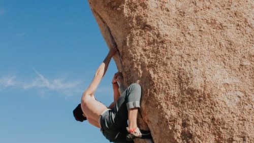 上半身裸でボルダリングの語源となる自然岩を登る男性