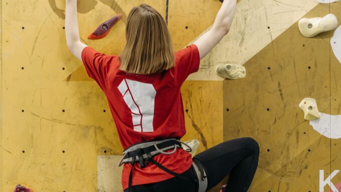 Tシャツとショートパンツ、スポーツタイツでボルダリングをする女性